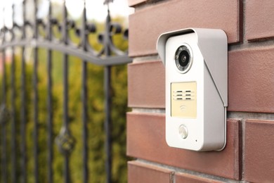 Modern intercom on red wall near gates outdoors, space for text