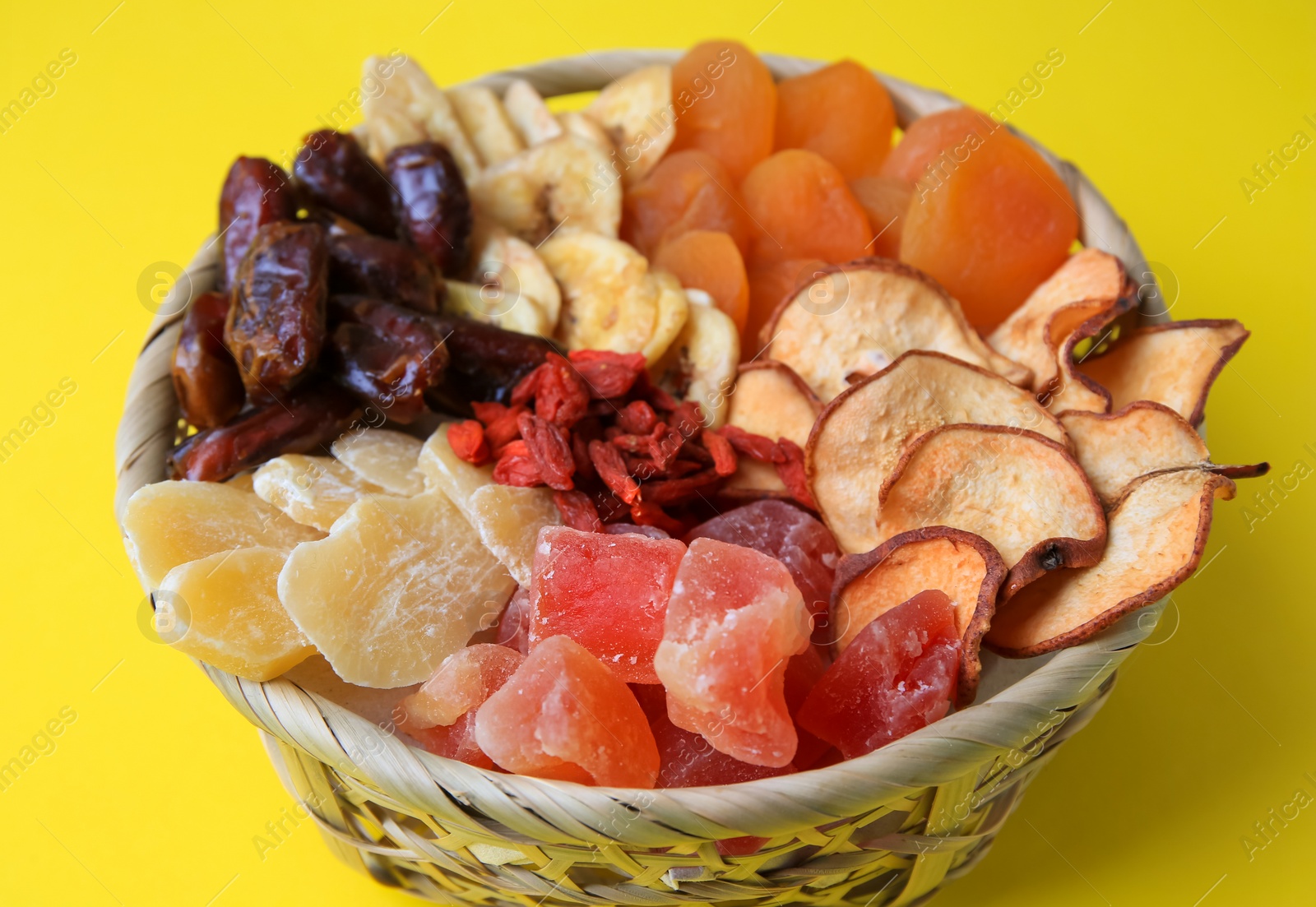 Photo of Wicker basket with different dried fruits on yellow background, closeup