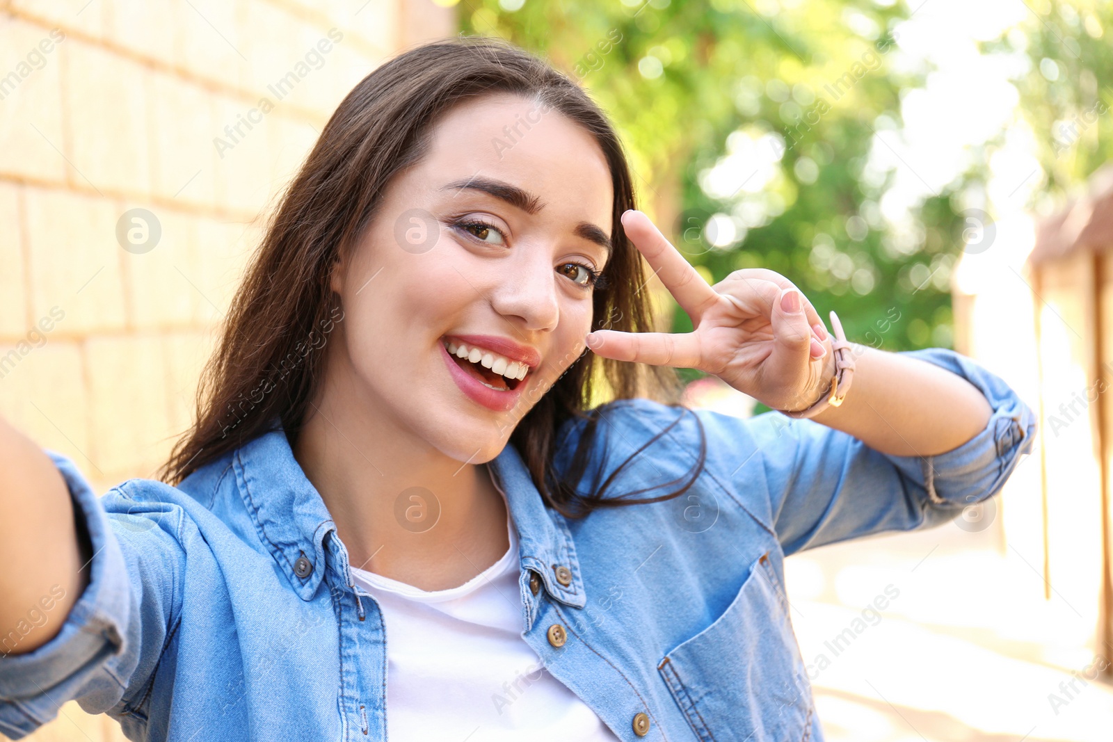 Photo of Young woman taking selfie outdoors on sunny day