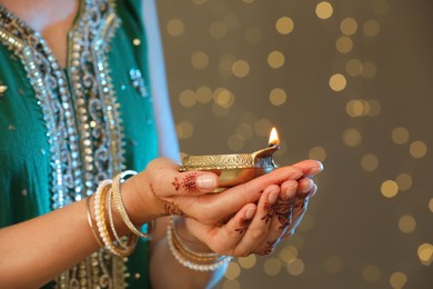 Photo of Woman holding lit diya lamp on brown background with blurred lights closeup view. Diwali holiday