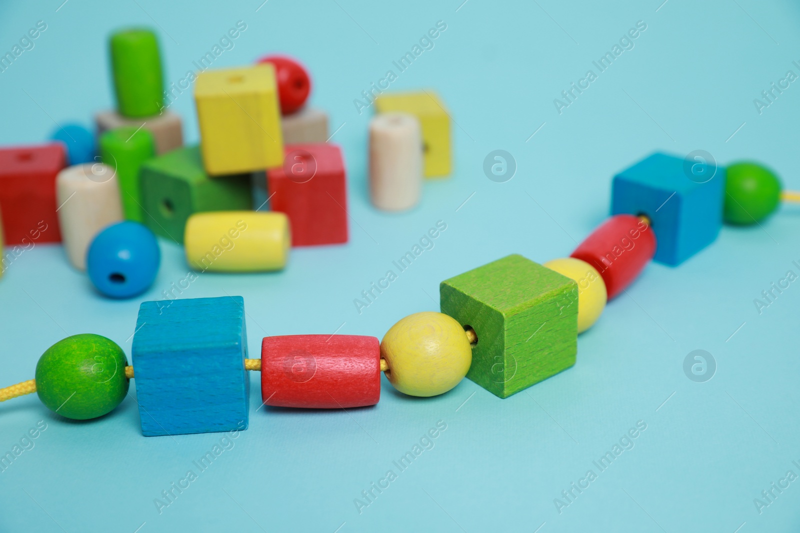 Photo of Wooden pieces and string for threading activity on light blue background, closeup. Educational toy for motor skills development