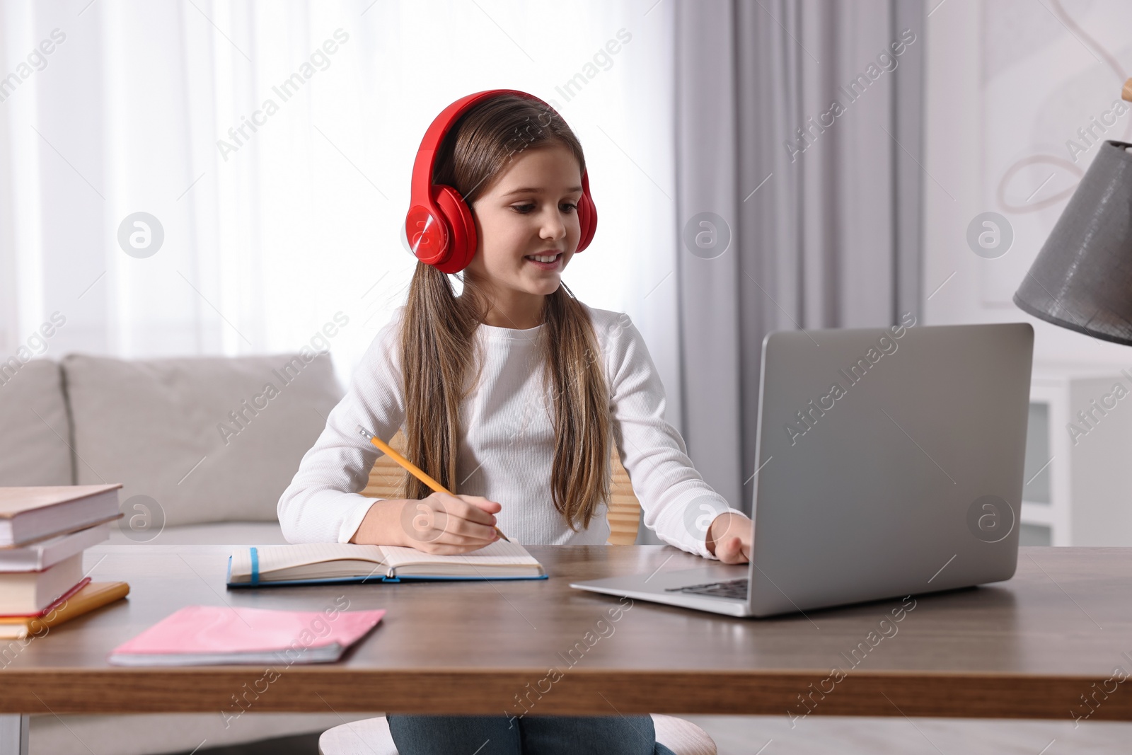 Photo of E-learning. Cute girl taking notes during online lesson at table indoors