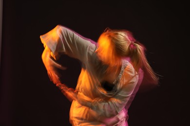 Photo of Young woman performing contemporary dance on black background, motion blur effect