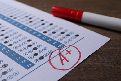 School grade. Answer sheet with red letter A, plus symbol and marker on wooden table, closeup