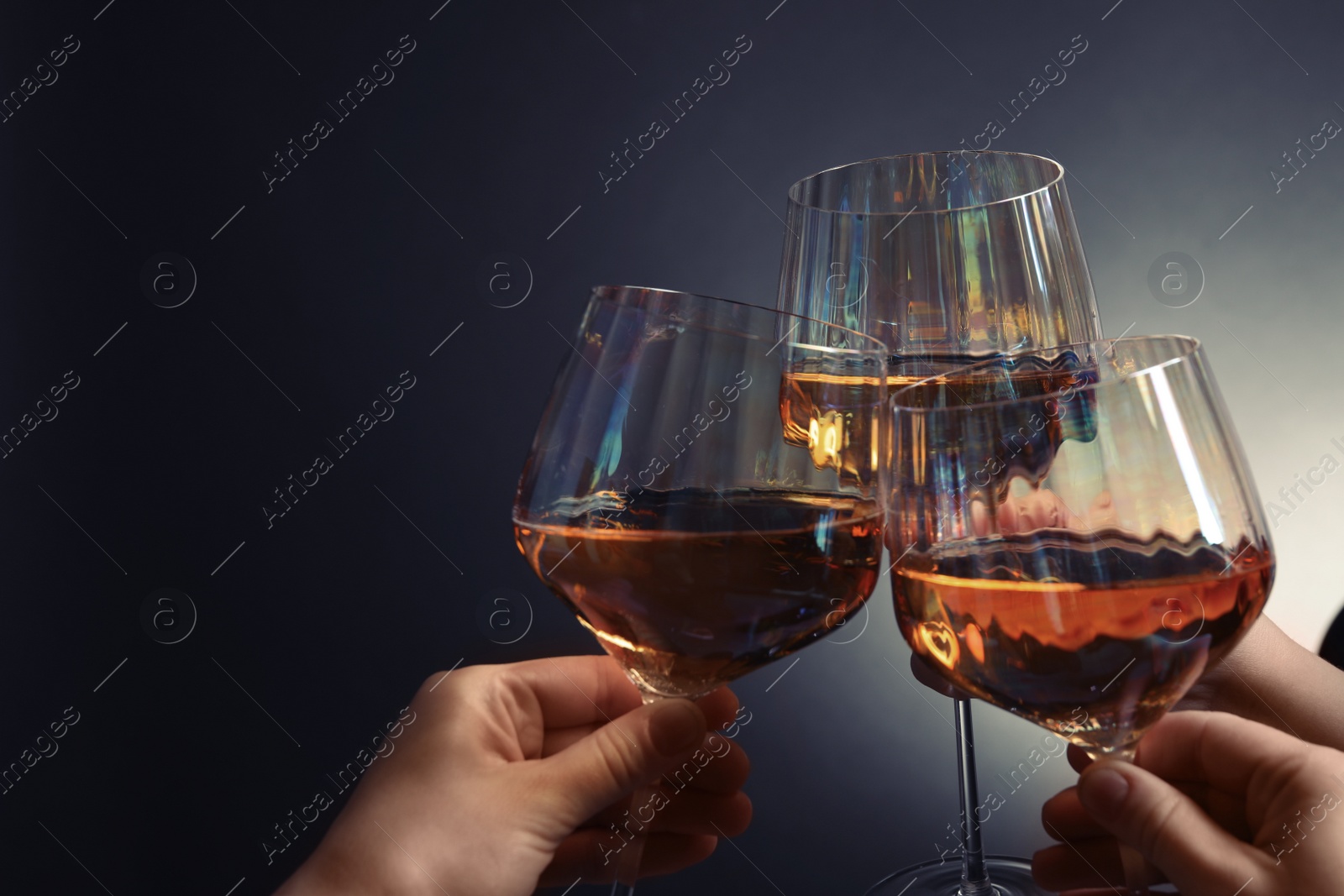 Photo of Women clinking glasses with white wine on dark background, closeup