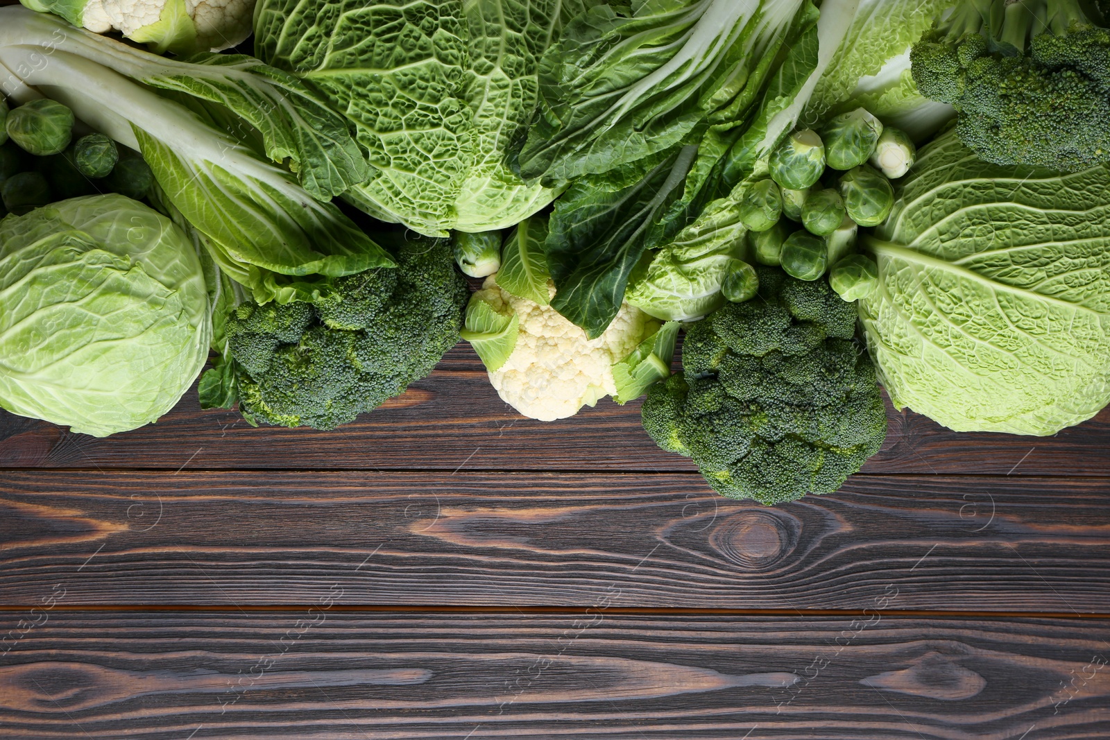 Photo of Many different types of fresh cabbage on wooden table, flat lay. Space for text