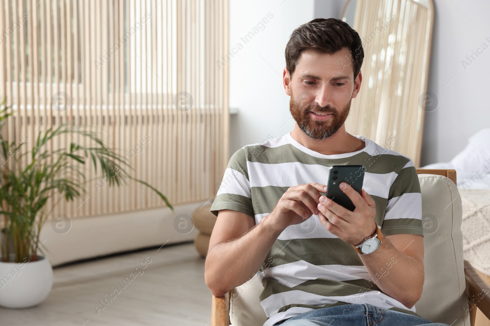 Photo of Handsome man using smartphone at home, space for text