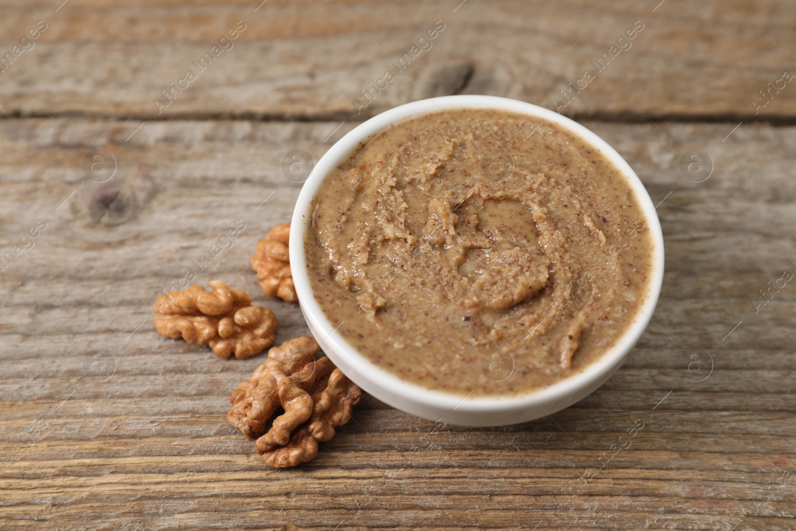 Photo of Delicious nut butter in bowl and walnuts on wooden table, closeup