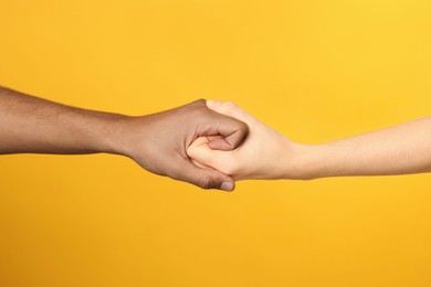 Photo of International relationships. People strongly joining hands on orange background, closeup