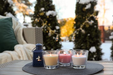 Photo of Beautiful burning candles and lantern on table outdoors. Cozy winter