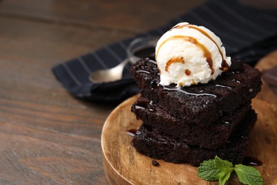Delicious brownies served with ice cream and caramel sauce on wooden table, closeup. Space for text