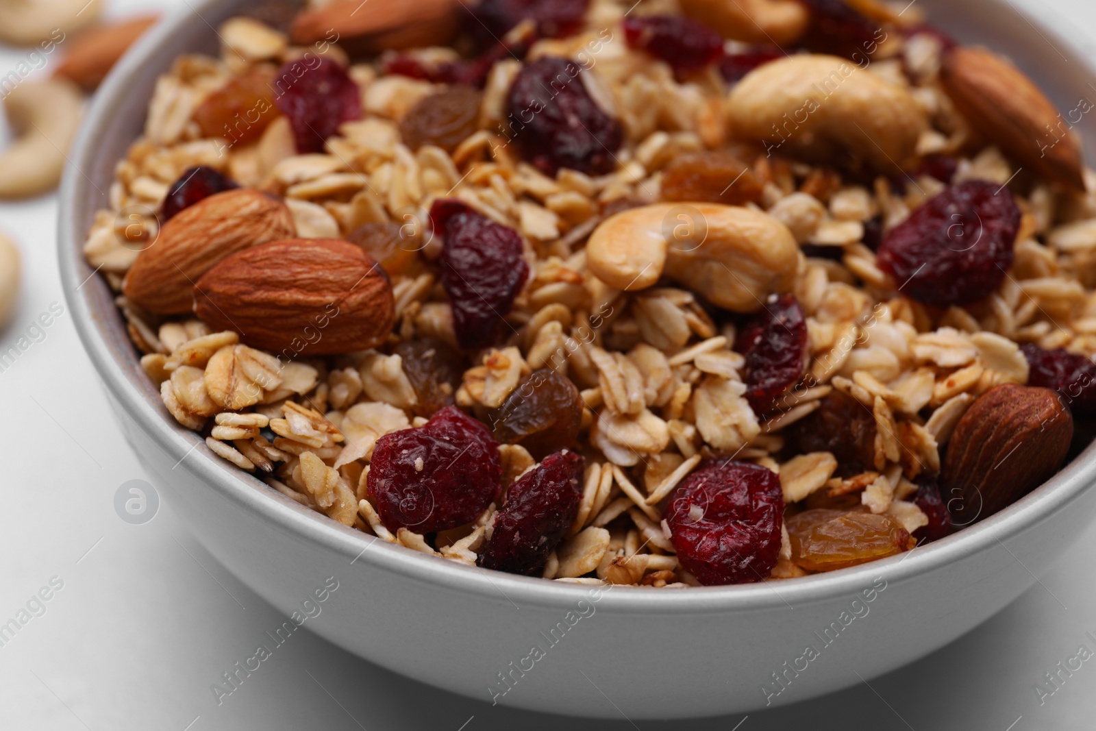 Photo of Bowl of tasty granola with nuts and dry fruits on white marble table, closeup