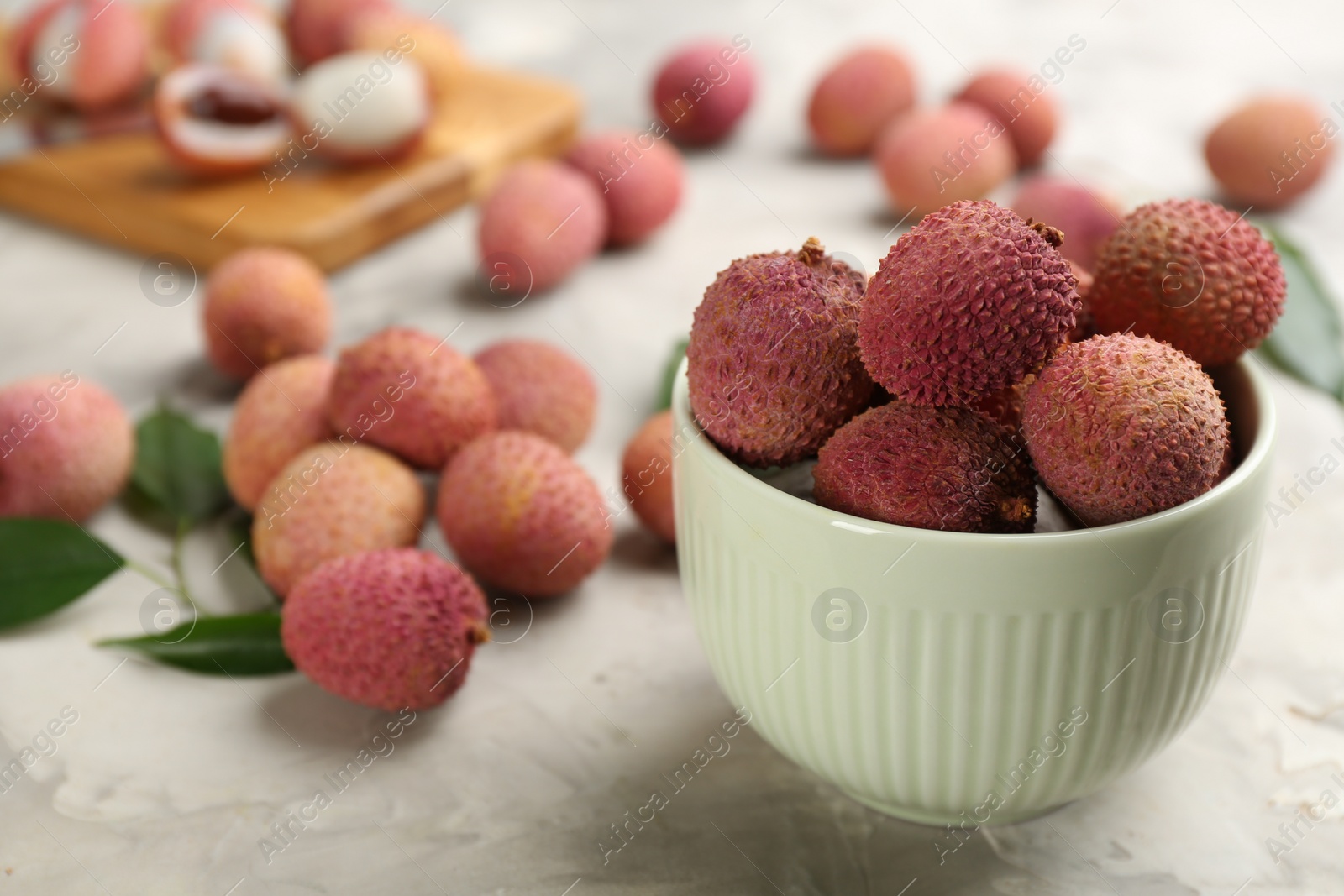 Photo of Fresh ripe lychee fruits in bowl on light grey table. Space for text