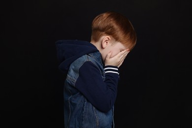Boy covering face with hands on black background. Children's bullying