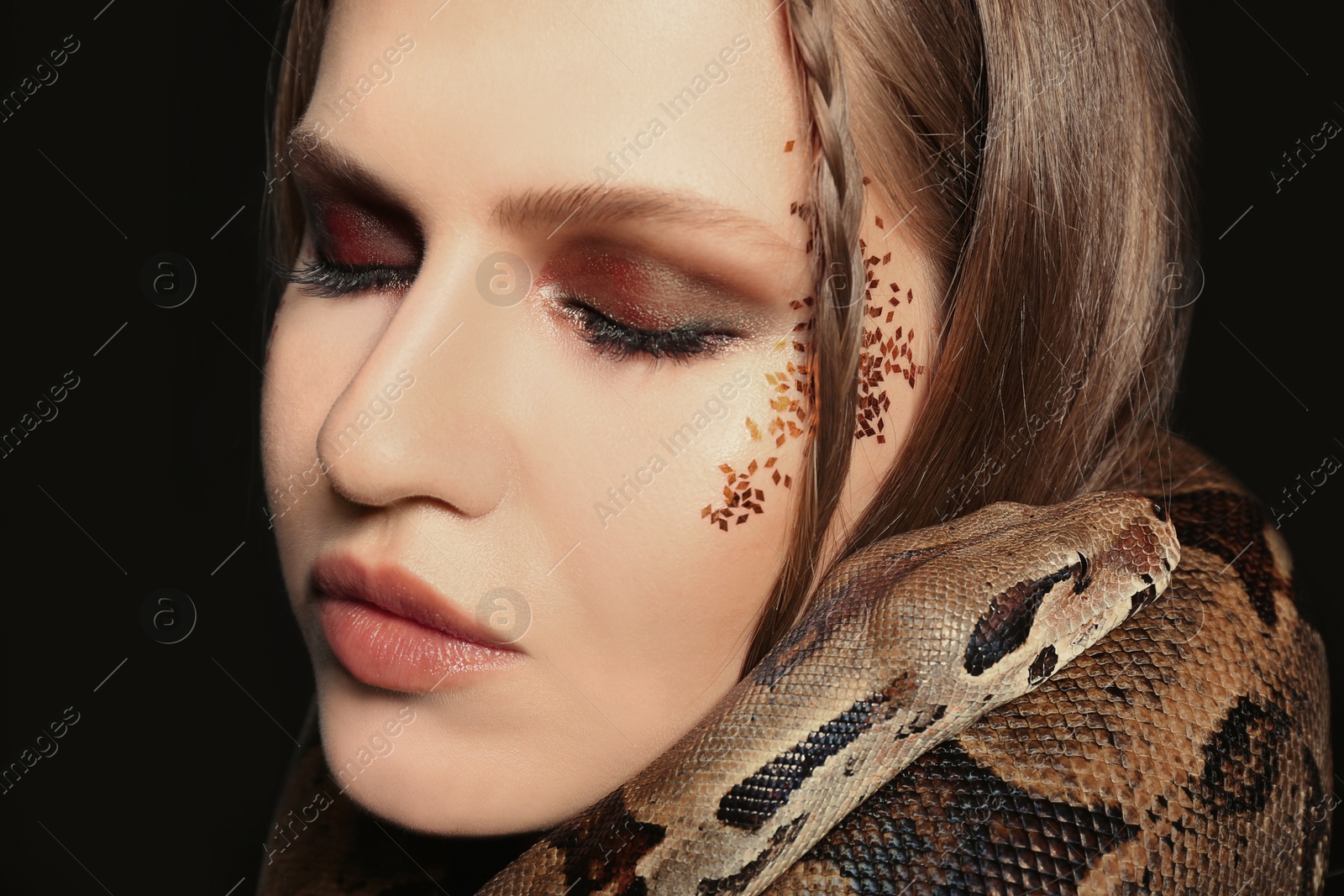 Photo of Beautiful woman with boa constrictor on black background, closeup