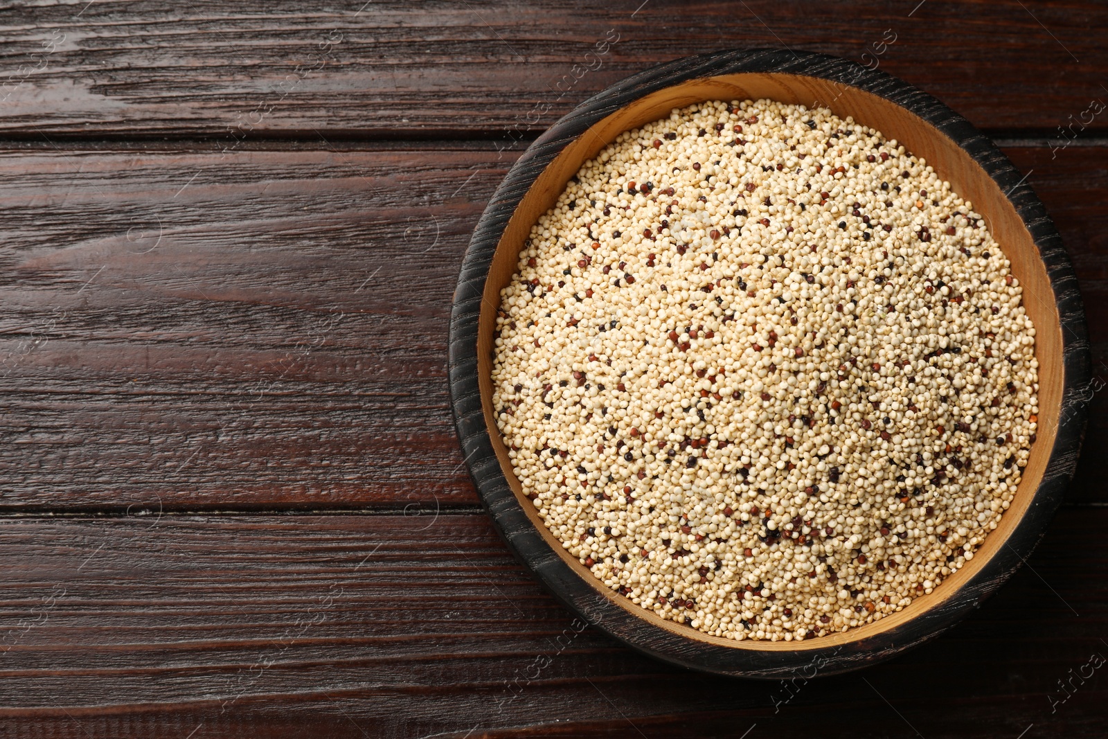 Photo of Raw quinoa seeds in bowl on wooden table, top view. Space for text