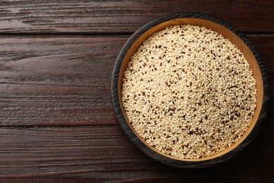 Photo of Raw quinoa seeds in bowl on wooden table, top view. Space for text