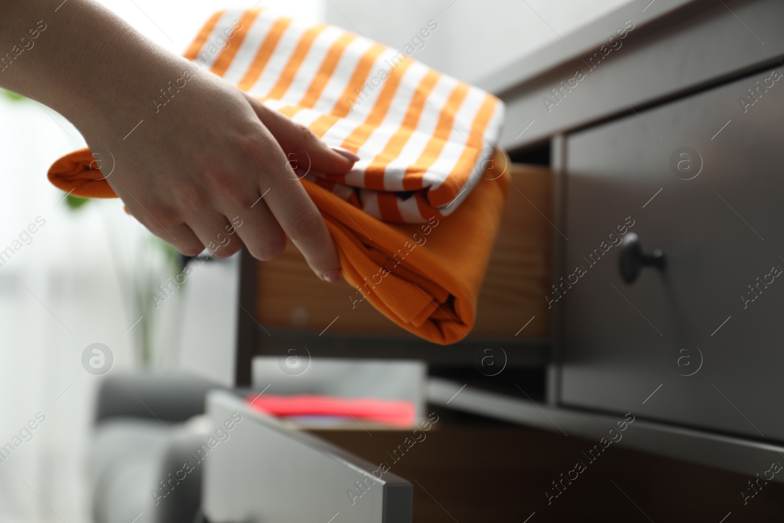 Photo of Woman putting folded clothes into drawer indoors, closeup