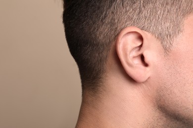 Photo of Man on beige background, closeup of ear. Space for text