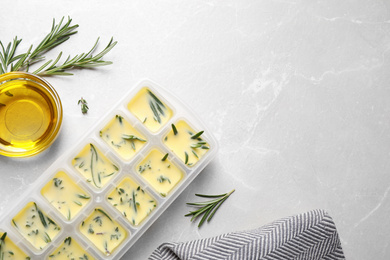 Photo of Ice cube tray with herbs frozen in oil and fresh rosemary on grey table, flat lay. Space for text