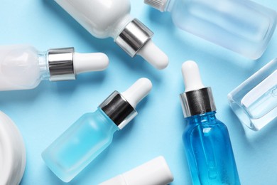 Photo of Many different bottles of cosmetic serum on light blue background, flat lay