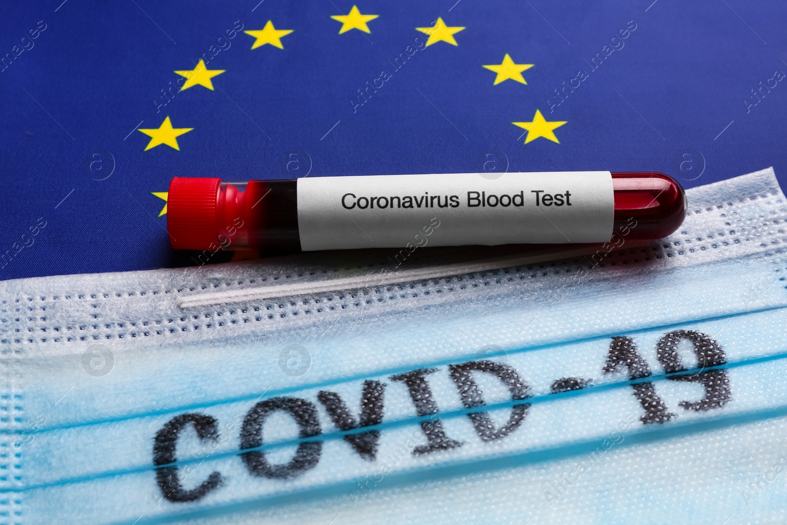 Photo of Protective mask and test tube with blood sample on European Union flag background, closeup. Coronavirus outbreak