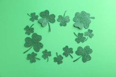 Photo of St. Patrick's day. Frame of shiny decorative clover leaves on green background, flat lay. Space for text