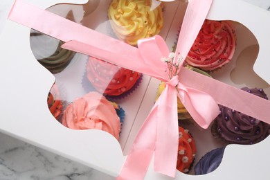 Photo of Different colorful cupcakes in box on table, closeup