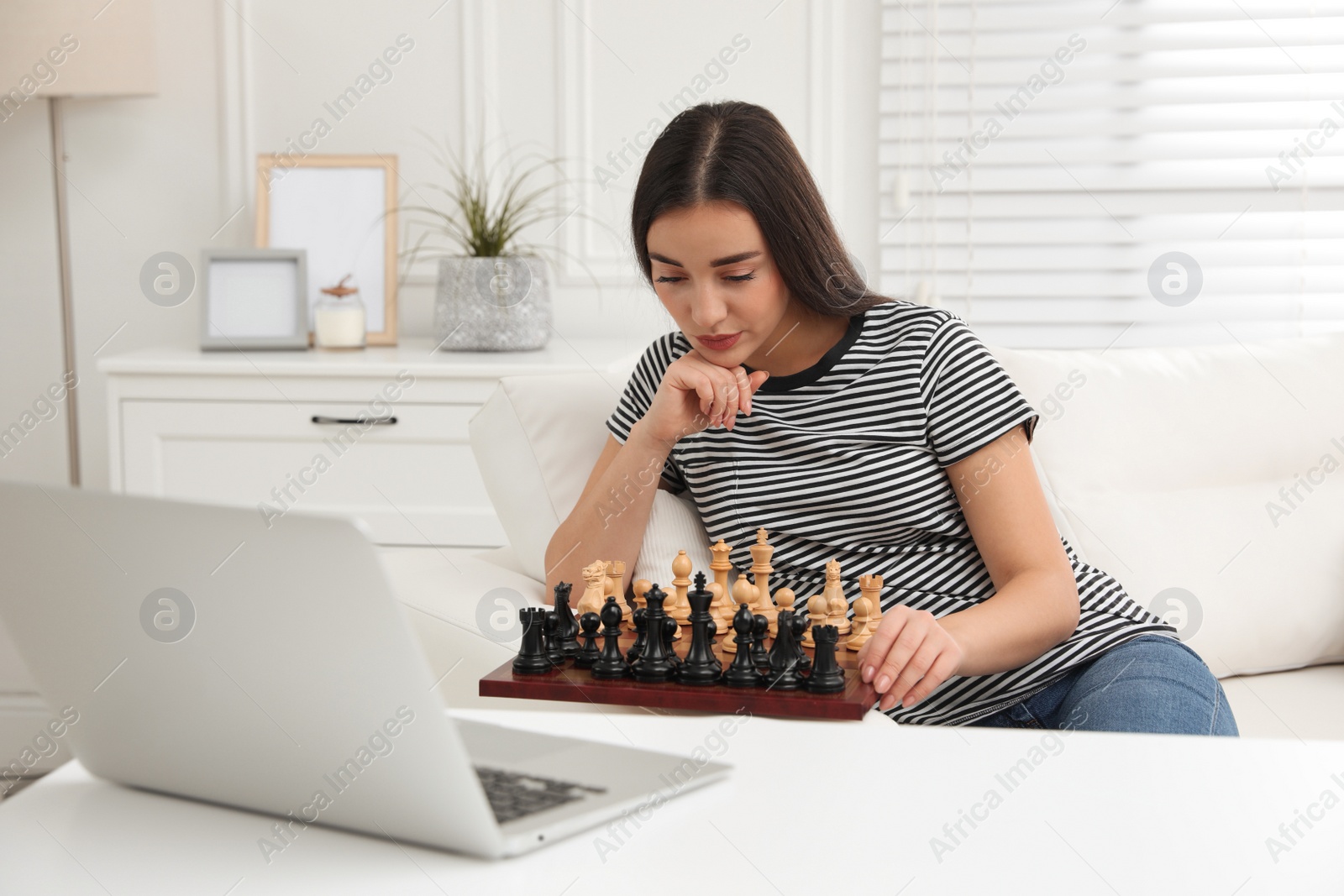 Photo of Young woman playing chess with partner through online video chat at home