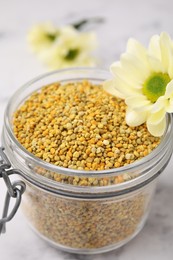 Photo of Fresh bee pollen granules in jar and flower on table, closeup