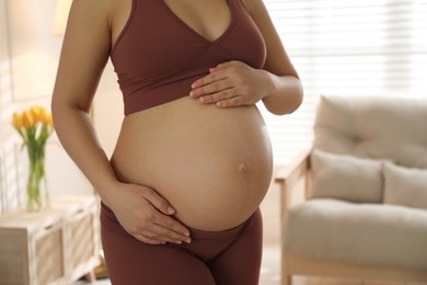 Pregnant young woman touching belly at home, closeup