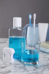 Fresh mouthwash in bottle, glass and dental floss on white marble table, closeup