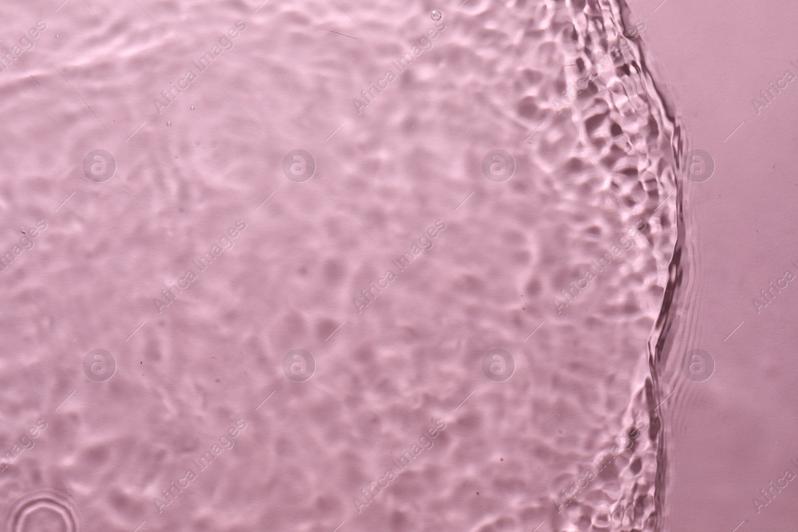 Photo of Rippled surface of clear water on pink background, top view