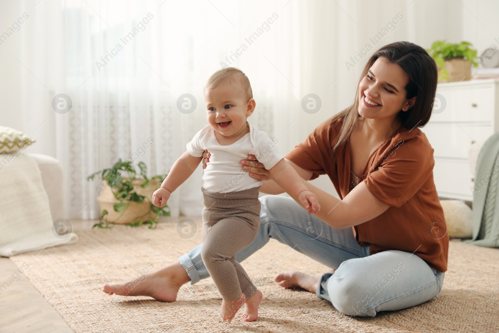 Photo of Mother supporting her baby daughter while she learning to walk at home