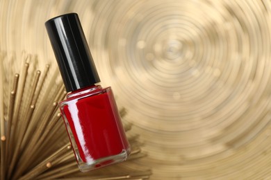 Photo of Stylish presentation of red nail polish in bottle on golden textured surface, closeup. Space for text
