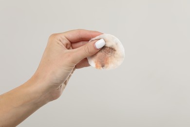 Woman with dirty cotton pad after removing makeup on light grey background, closeup