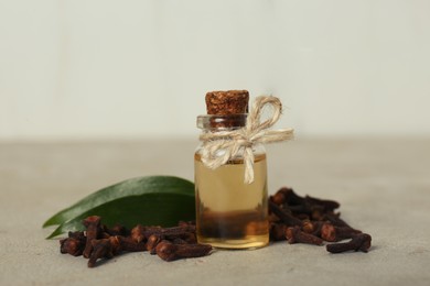 Photo of Essential oil, dried cloves and green leaves on light grey table