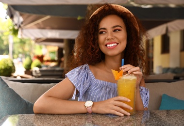 Happy African-American woman with glass of natural lemonade in cafe. Detox drink