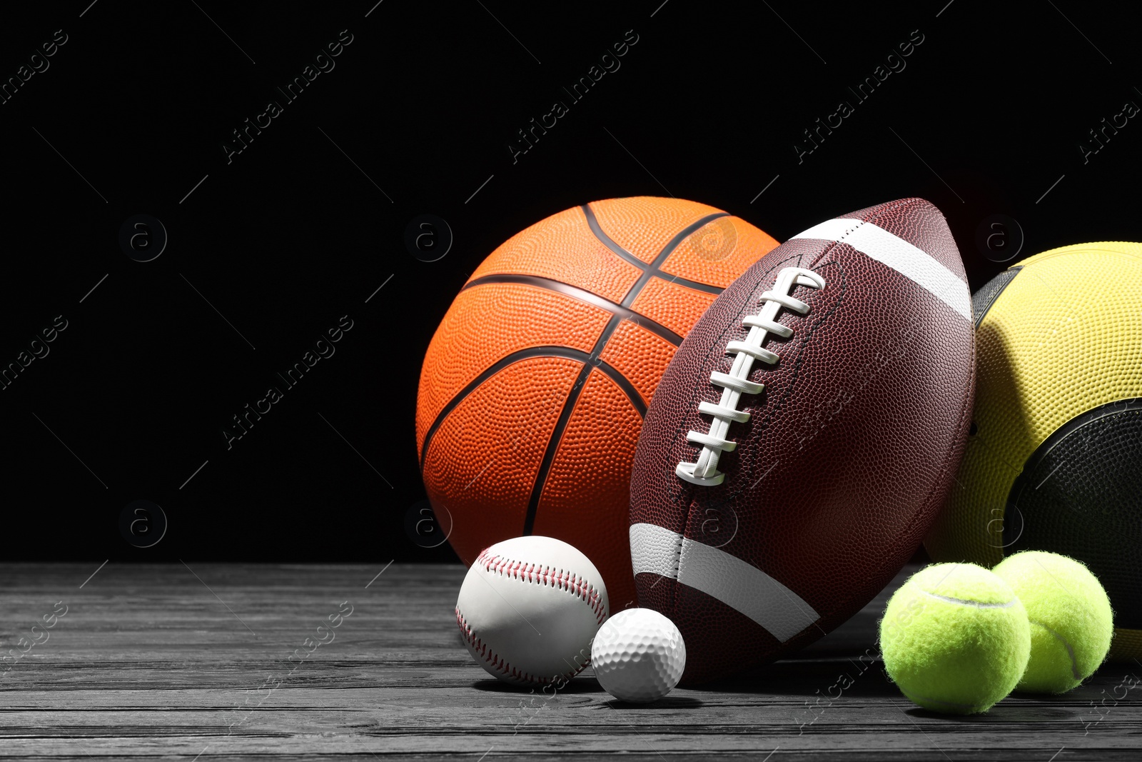 Photo of Many different sport balls on dark wooden table against black background, space for text