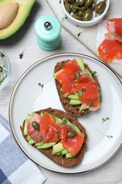 Photo of Delicious sandwiches with salmon, avocado and capers on white wooden table, flat lay