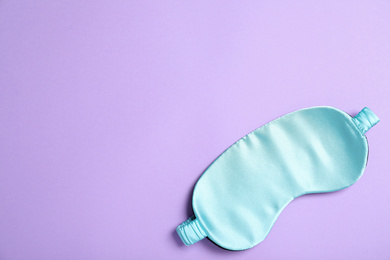 Photo of Light blue sleeping mask on violet background, top view with space for text. Bedtime accessory