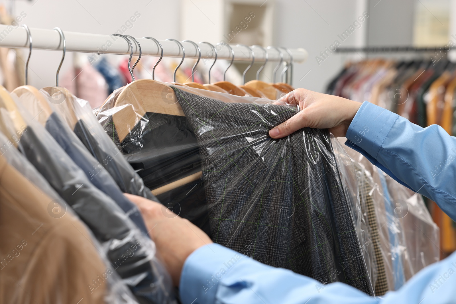 Photo of Dry-cleaning service. Woman taking jacket in plastic bag from rack indoors, closeup