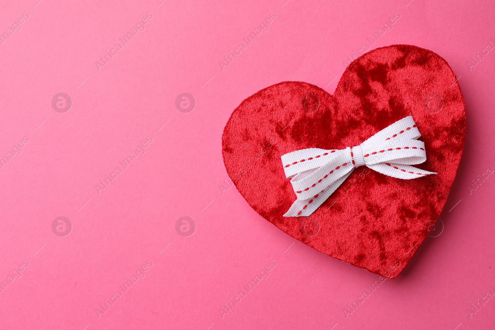 Photo of Red textile heart with white bow on pink background, top view. Space for text