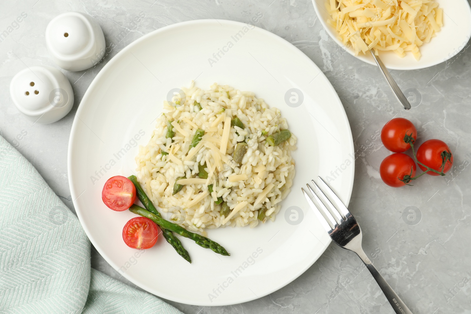Photo of Delicious risotto with asparagus and tomatoes on grey marble table, flat lay