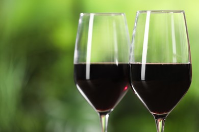 Tasty red wine in glasses against blurred green background, space for text