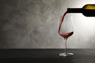 Pouring red wine from bottle into glass on table. Space for text