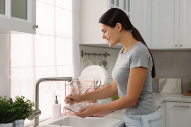 Photo of Happy woman washing glass at sink in kitchen