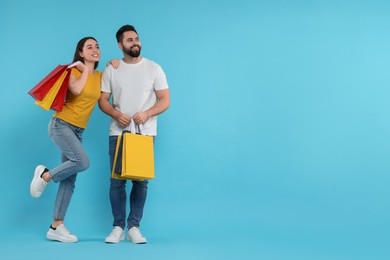 Happy couple with shopping bags on light blue background. Space for text
