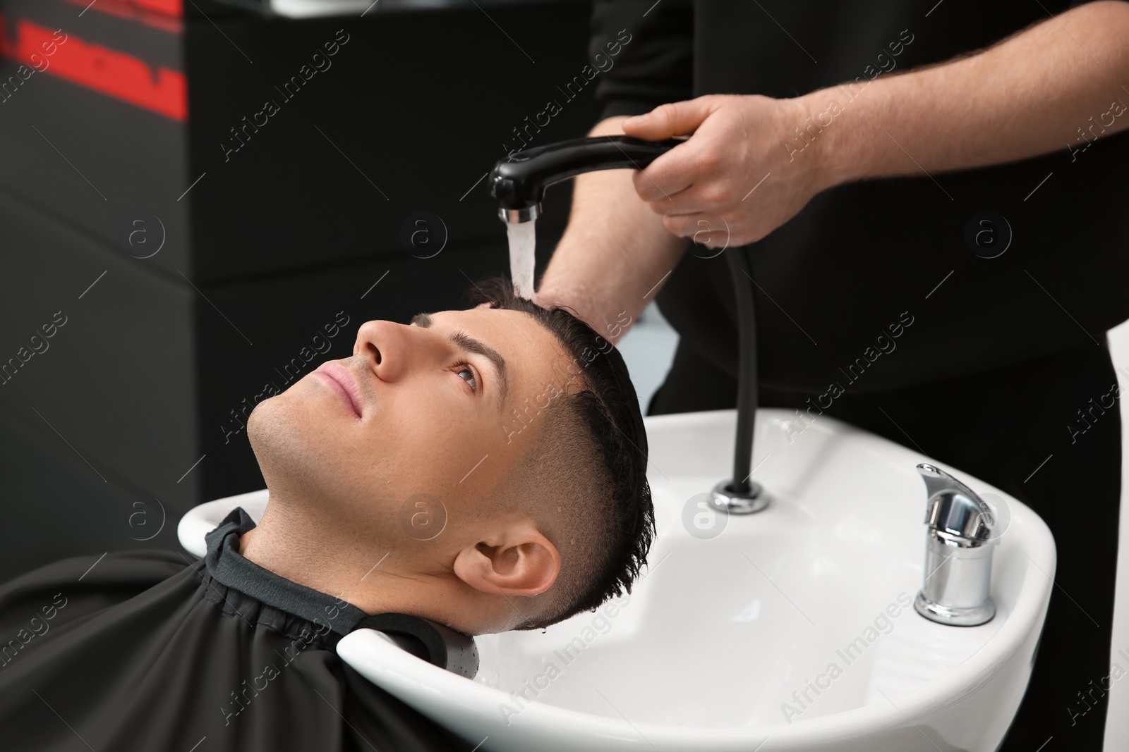 Photo of Professional barber washing client's hair at sink in salon, closeup