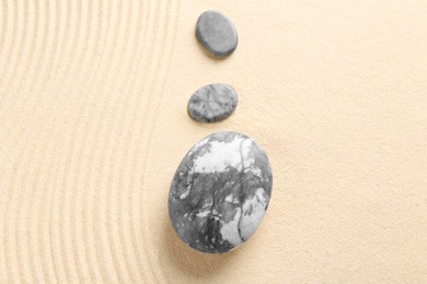 Photo of Zen garden stones on beige sand with pattern, flat lay